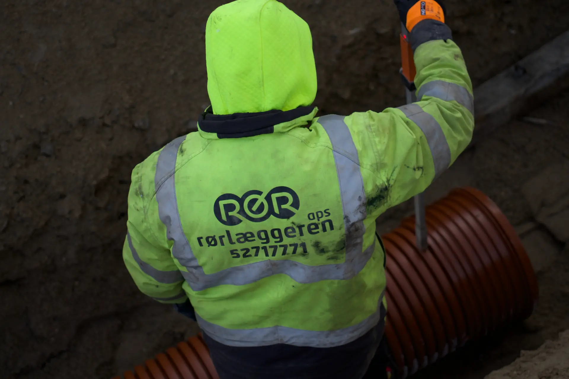 Rørlægger i højt synligt arbejdstøj med rør.
