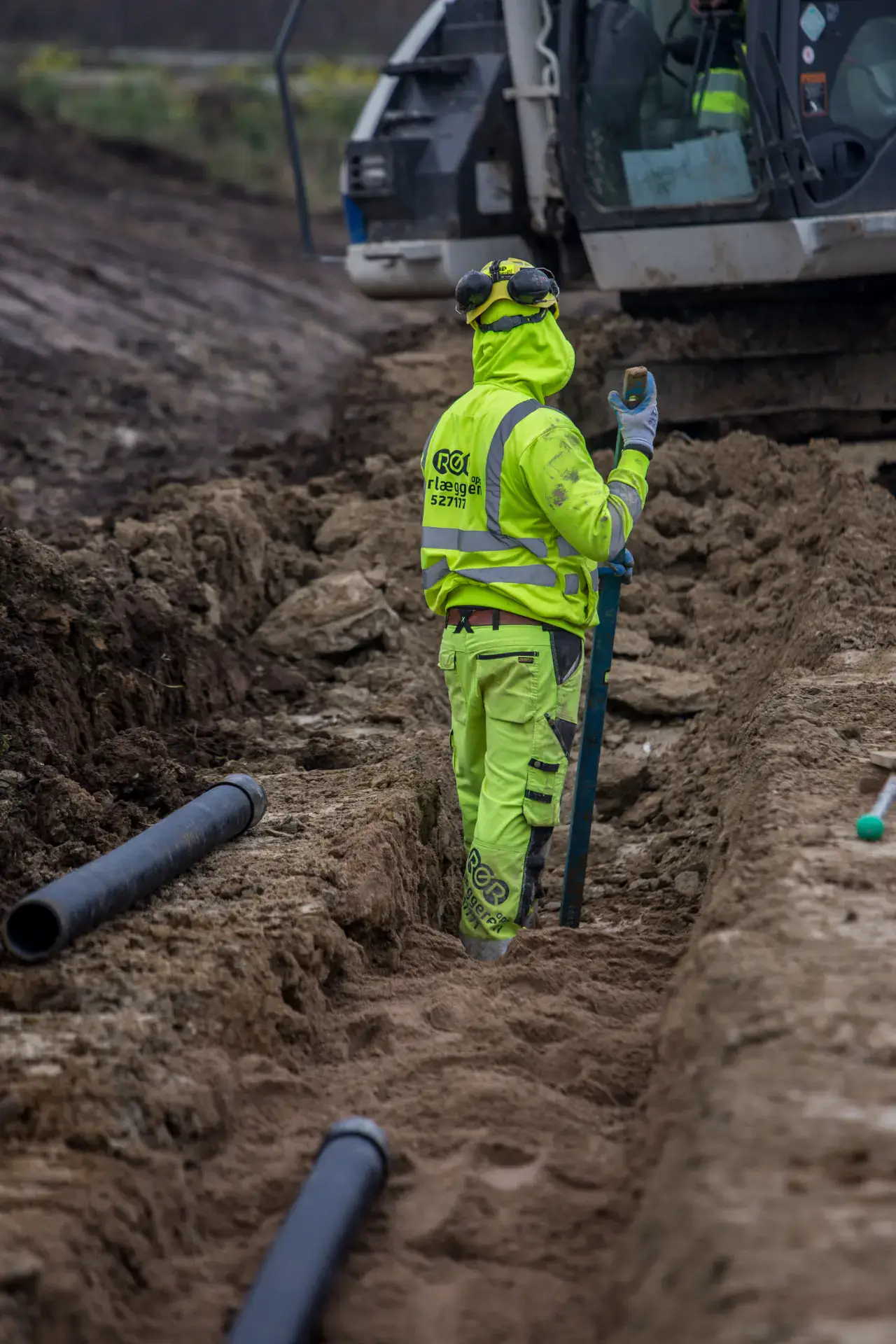 Rørlægger arbejder med kloakrør i jord under byggeprojekt.